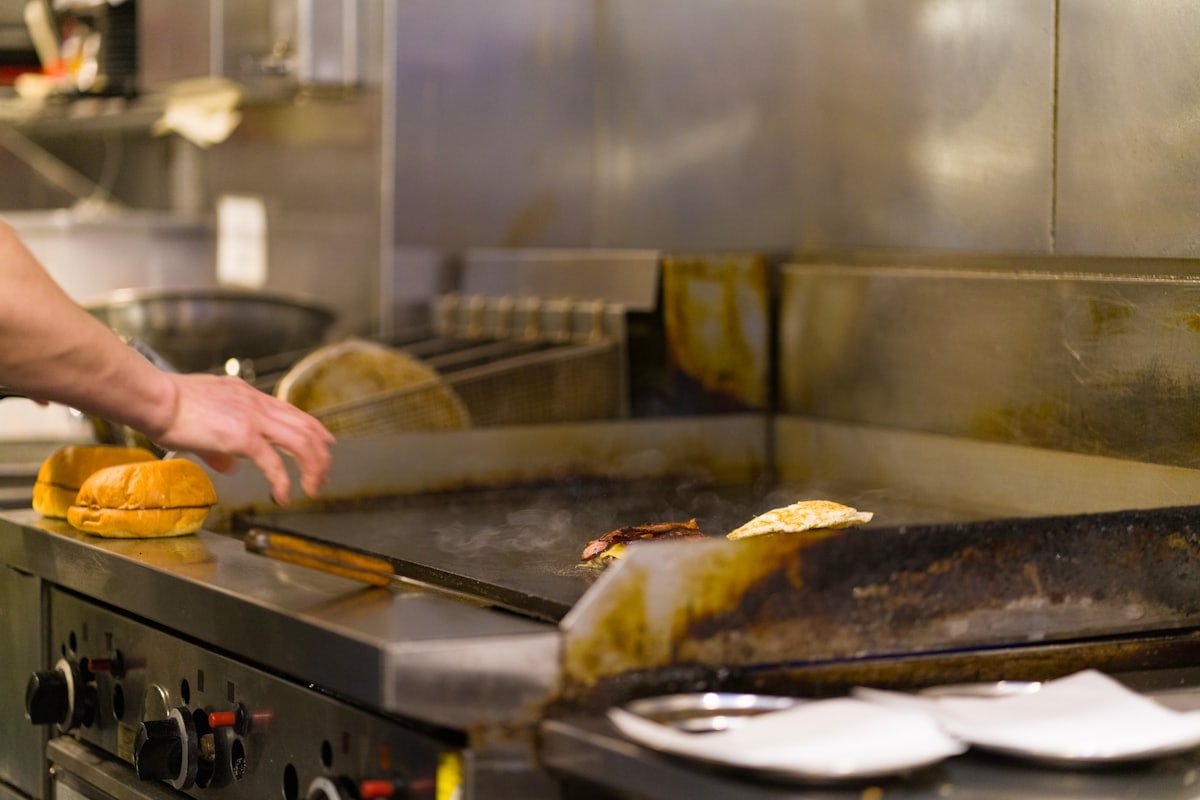 A chef preparing food on a commercial gas grill in a food business kitchen